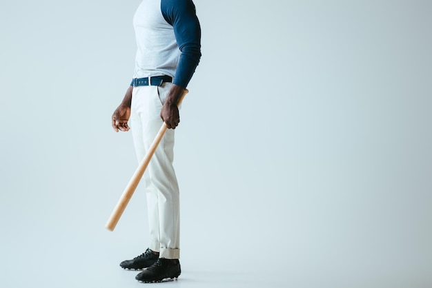 Vista parziale dello sportivo afroamericano con mazza da baseball su sfondo grigio