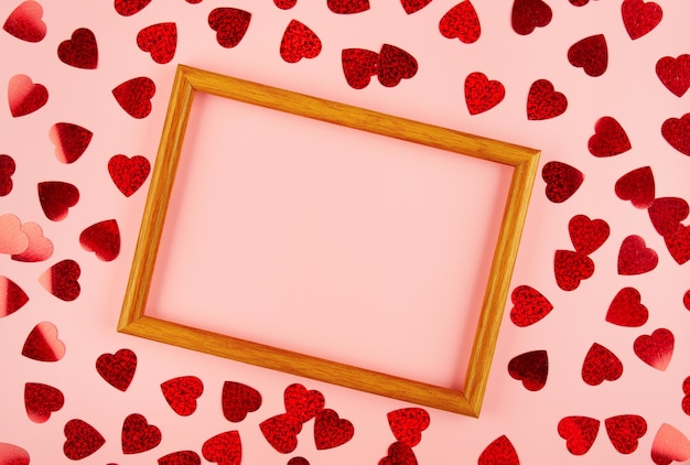 Vista piatta sul telaio di legno tra orpelli a forma di cuore su sfondo rosa