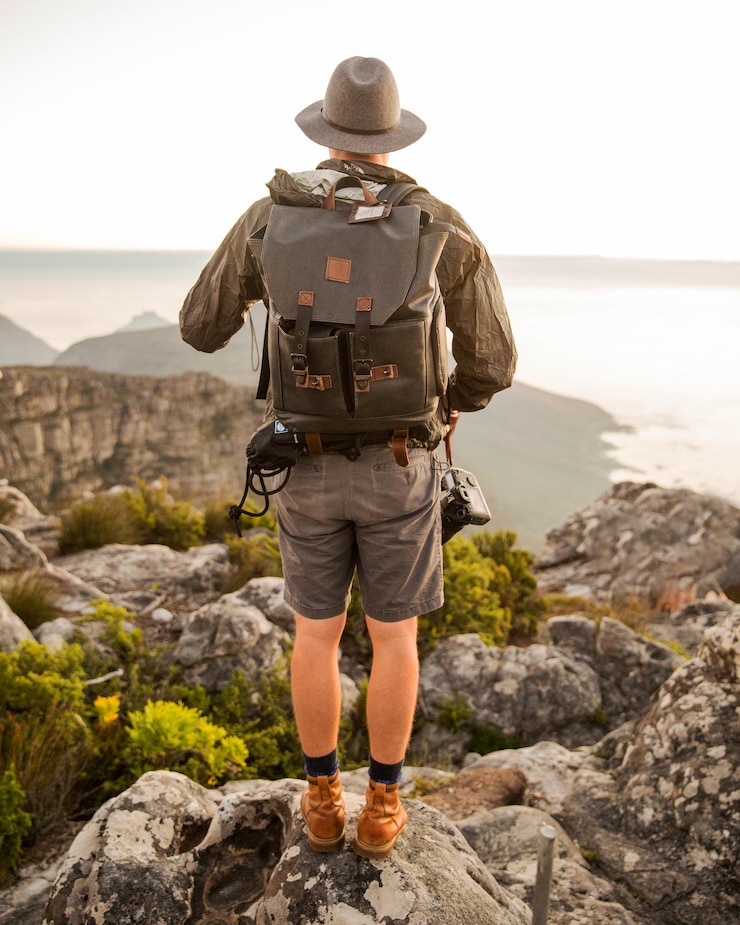 Foto vista posteriore a tutta lunghezza di un uomo con uno zaino che cammina su montagne rocciose contro il mare