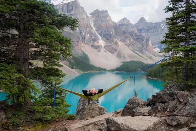 Vista posteriore ad alto angolo di un uomo che riposa su un'amaca di fronte al lago in un paesaggio montuoso