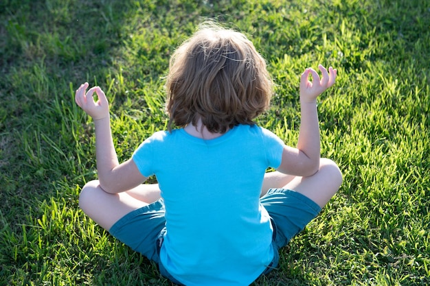 Vista posteriore del bambino che medita sul lago al tramonto yoga sulla consapevolezza della natura bambino meditare nel parco estivo