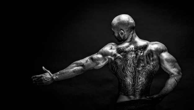 Vista posteriore del bodybuilder tatuato con il braccio teso