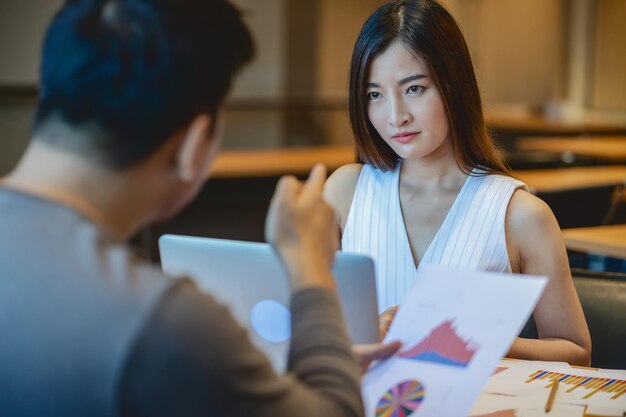 Vista posteriore del capo furioso che rimprovera una giovane donna d'affari asiatica in abito casual