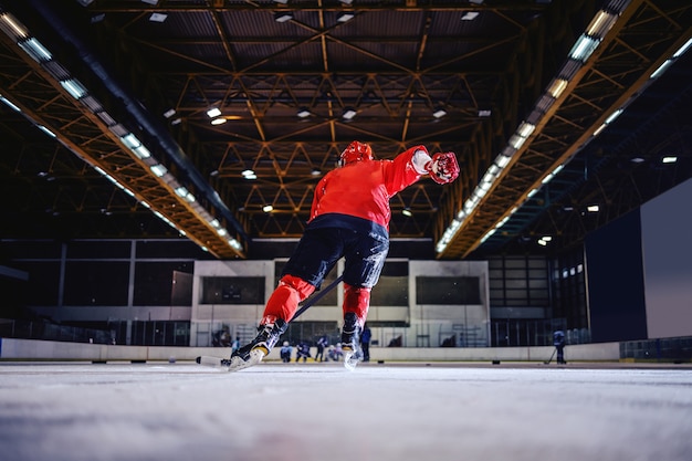 Vista posteriore del giocatore di hockey che pattina verso la squadra opposta e cerca di segnare. Interno della sala.