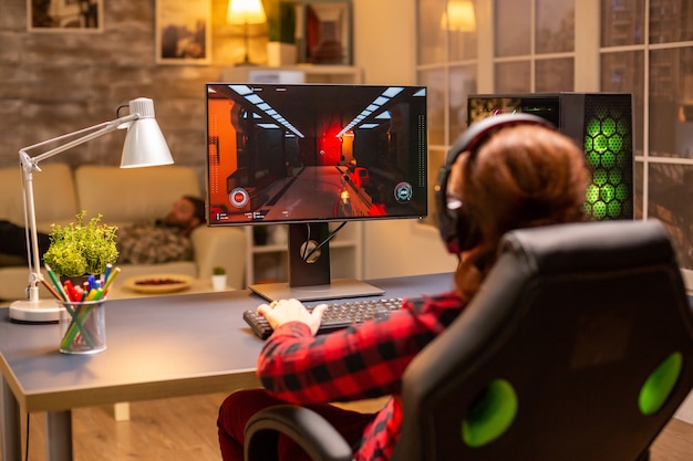 Vista posteriore del giocatore femminile che gioca su un potente computer PC a tarda notte nel soggiorno.