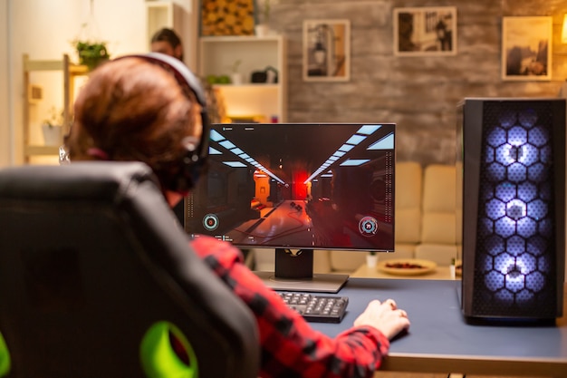 Vista posteriore del giocatore femminile che gioca su un potente computer PC a tarda notte nel soggiorno.