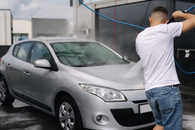 Vista posteriore del giovane che pulisce la sua auto con un autolavaggio self-service con spruzzatore a getto