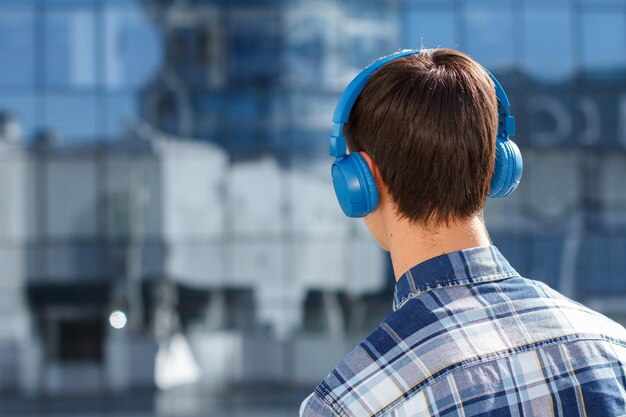 Vista posteriore del giovane in camicia a scacchi con cuffie wireless in città