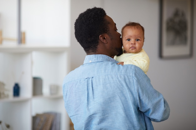 Vista posteriore del giovane padre africano tenendo la bambina sulle sue mani e baciandola