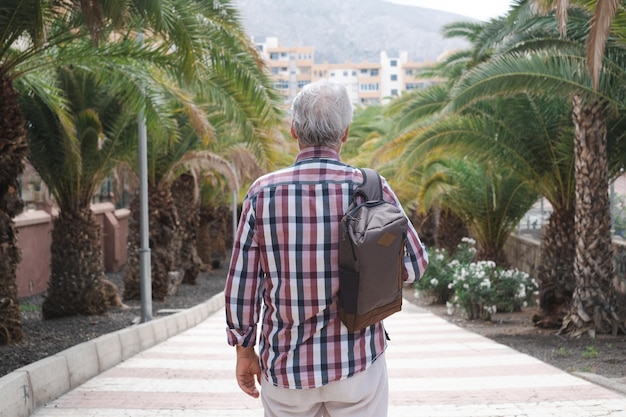 Vista posteriore del maschio turistico senior con uno zaino che cammina per strada a Tenerife godendosi viaggi e vacanze