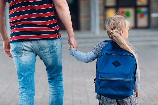 Vista posteriore del padre che torna a scuola con sua figlia che trasporta lo zaino.