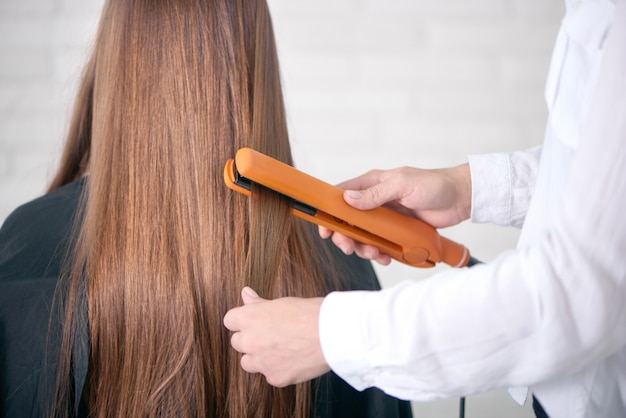 Vista posteriore del parrucchiere che raddrizza i lunghi capelli castani del cliente.