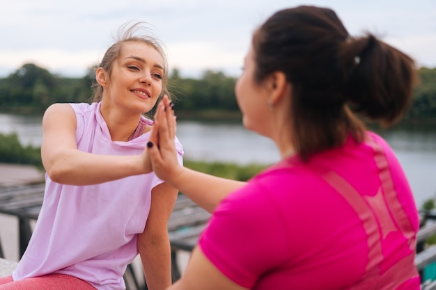 Vista posteriore del primo piano di un'istruttrice di fitness positiva e di una giovane donna grassa motivata che si salutano