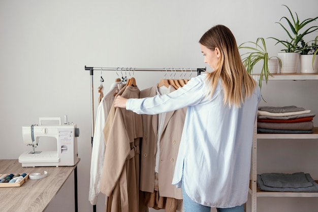 Vista posteriore del sarto femminile che controlla gli indumenti sui ganci