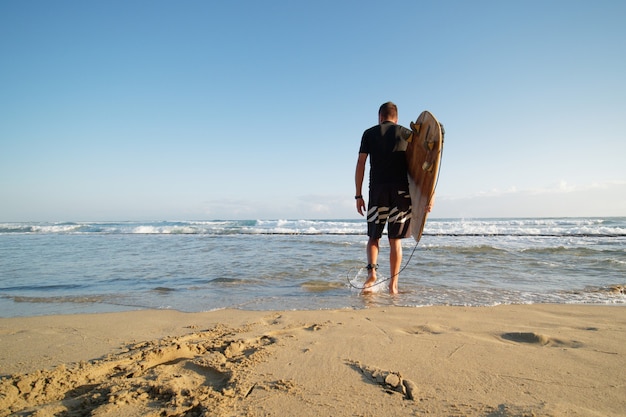 Vista posteriore del surfista uomo con la tavola da surf che va all'oceano. Stile di vita.