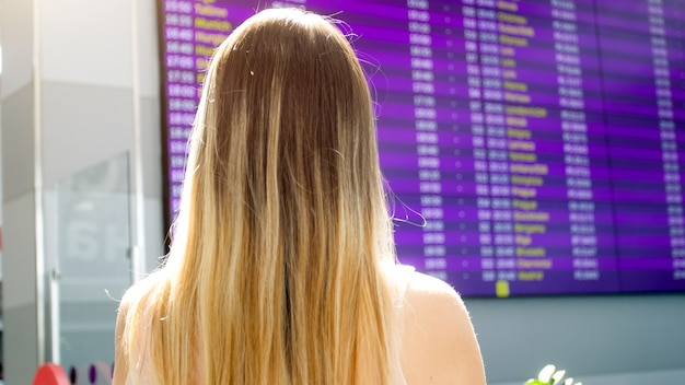 Vista posteriore del turista femminile alla ricerca sulla scheda di pianificazione delle informazioni in aeroporto.