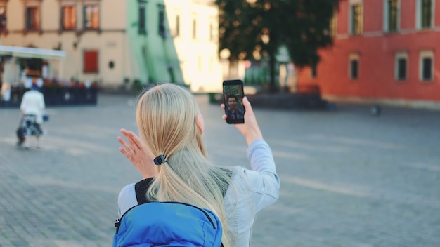 Vista posteriore del turista femminile che effettua videochiamata su smartphone con la sua amica da un altro luogo