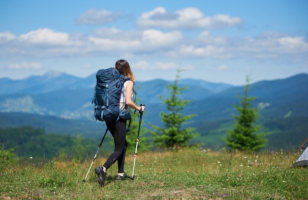 Vista posteriore del viaggiatore femminile attivo con zaino e bastoncini da trekking