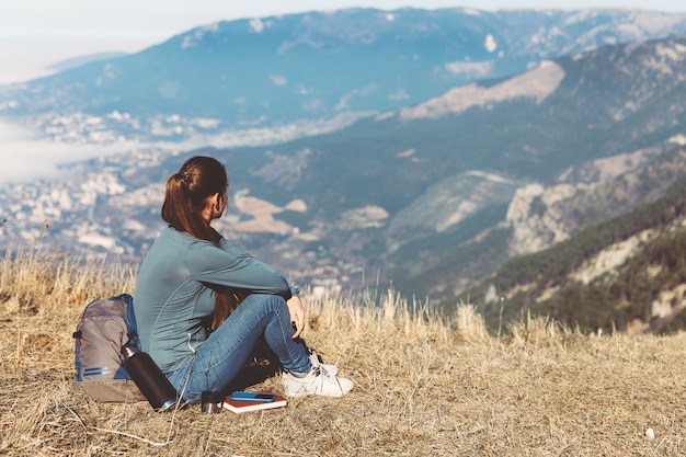 Vista posteriore del viaggio donna. Giovane bella ragazza viaggia da sola in montagna in primavera o in autunno, si siede sul bordo della montagna e guarda in lontananza