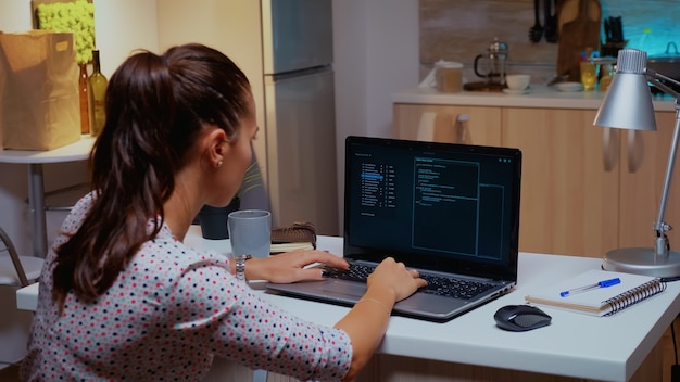 Vista posteriore dell'hacker donna che codifica un virus pericoloso per attaccare il database aziendale a mezzanotte. Programmatore che scrive un malware pericoloso per attacchi informatici utilizzando il dispositivo ad alte prestazioni a tarda notte.