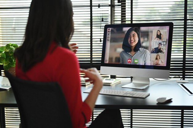 Vista posteriore dell'imprenditrice femminile che ha una videochiamata che discute problemi in remoto online con diversi colleghi sul computer