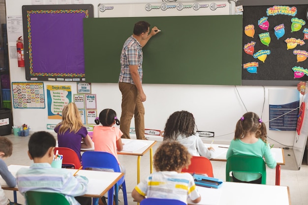 Vista posteriore dell'insegnante che scrive sulla lavagna con un pezzo di gesso