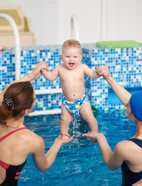 Vista posteriore dell'istruttore di nuoto e della madre che sollevano il ragazzino sopra l'acqua blu della piscina che insegna al bambino in piedi