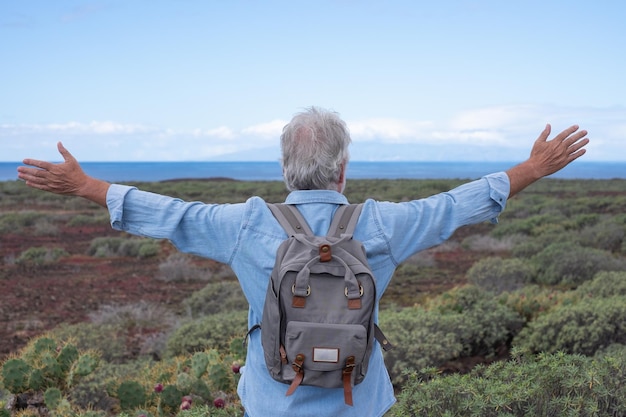 Vista posteriore dell'uomo anziano con le braccia aperte in una giornata di trekking nel sentiero di campagna di fronte al mare