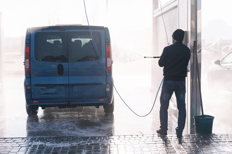 Vista posteriore dell'uomo che pulisce la sua auto con un lavaggio auto self service con spruzzatore a getto