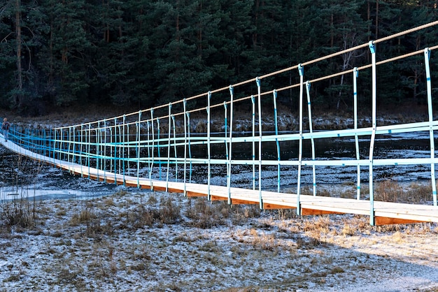 Vista posteriore dell'uomo con lo zaino che cammina sul ponte di legno innevato attraverso il fiume nella foresta di autunno inverno