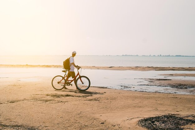 vista posteriore dell'uomo con zaino in piedi e che tiene la bicicletta sul lungomare