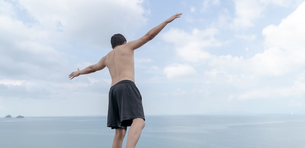 Vista posteriore dell'uomo ha aperto le mani con gioia all'oceano e al cielo.