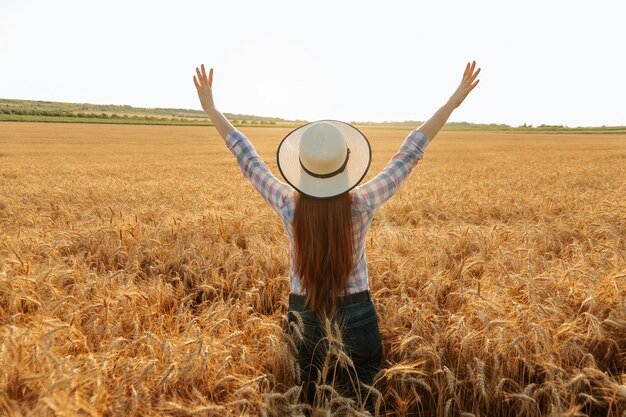 Vista posteriore della contadina con cappello in testa in un campo di grano dorato al tramonto tempo del raccolto estate soleggiata...