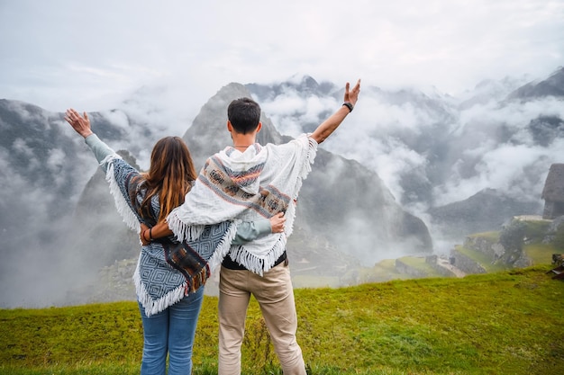 Vista posteriore della coppia caucasica che indossa il poncho peruviano e alza le braccia davanti a Machu Picch