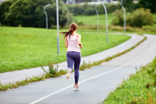 Vista posteriore della donna che corre sulla strada al mattino d'estate