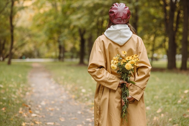 Vista posteriore della donna con bouquet di fiori nel parco in autunno