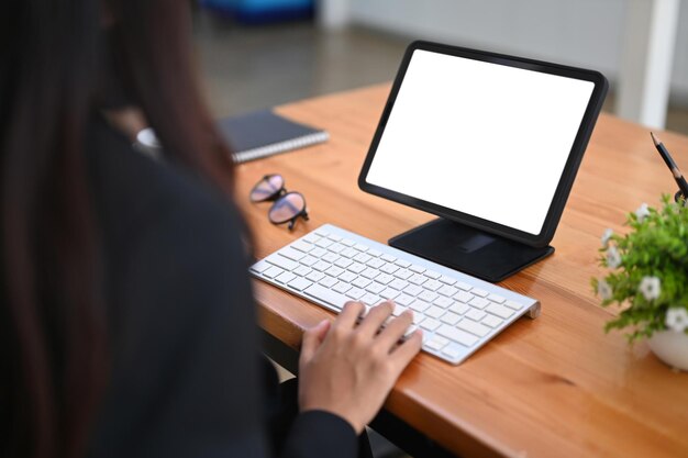 Vista posteriore della donna d'affari che digita sulla tastiera wireless mentre si lavora con la tavoletta digitale