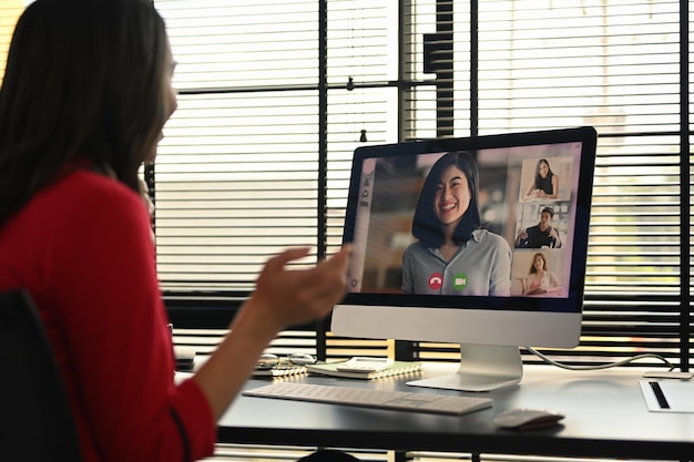 Vista posteriore della donna d'affari che ha una videochiamata che discute di problemi in remoto online con diversi colleghi