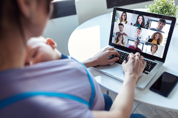 Vista posteriore della donna e del suo bambino che fanno riunioni online con i colleghi in videochiamata sul laptop a casa.