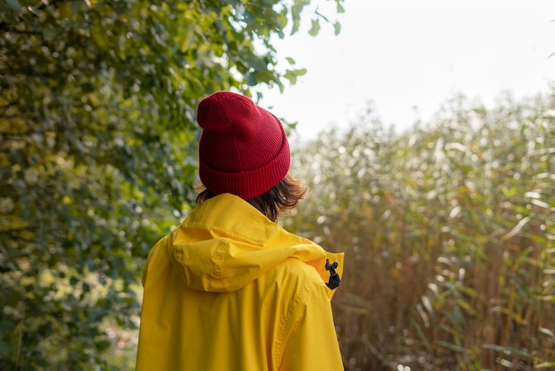 Vista posteriore della donna in impermeabile giallo brillante e cappello rosso guarda la canna