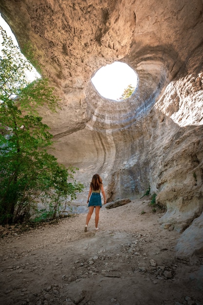 Vista posteriore della donna in piedi in una grotta sotterranea con un'apertura verso l'esterno