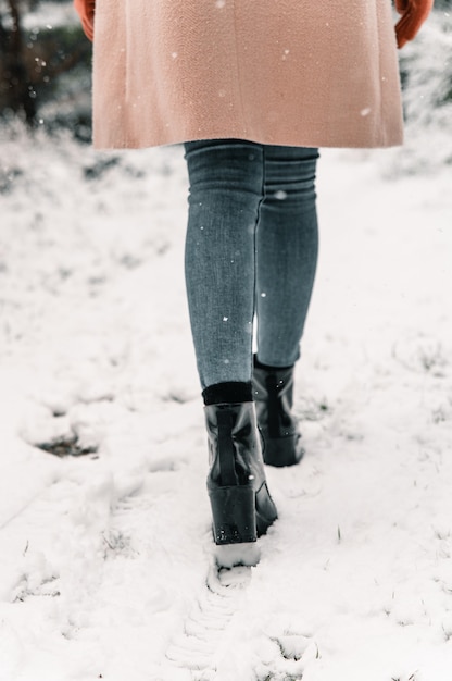 Vista posteriore della donna senza volto raccolto in cappotto caldo che cammina lungo il sentiero innevato nei boschi in giornata invernale