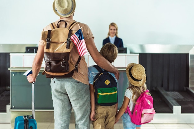 vista posteriore della famiglia con gli zaini che vanno al banco del check-in in aeroporto