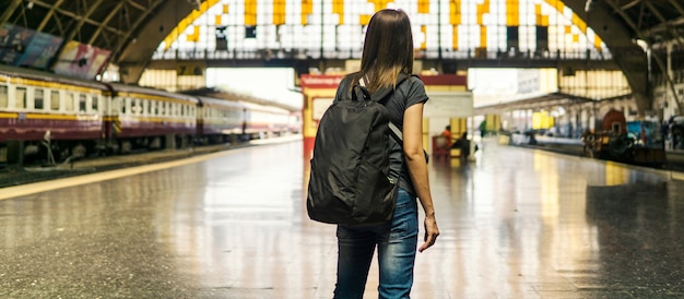 Vista posteriore della giovane donna asiatica viaggiatore con piccolo zaino sulla ferrovia stantion.in attesa per il treno per il trasporto in viaggio di vacanza.Concetto di viaggio