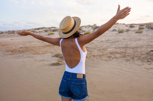 Vista posteriore della giovane donna che indossa un cappello e pantaloncini in spiaggia