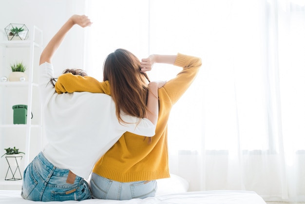 Vista posteriore delle coppie felici lesbiche delle donne che svegliano nella mattina, sedentesi sul letto