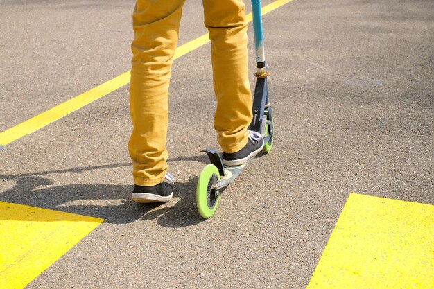 Vista posteriore delle gambe di un ragazzo in pantaloni gialli e stivali di gomma neri sullo scooter Primo piano