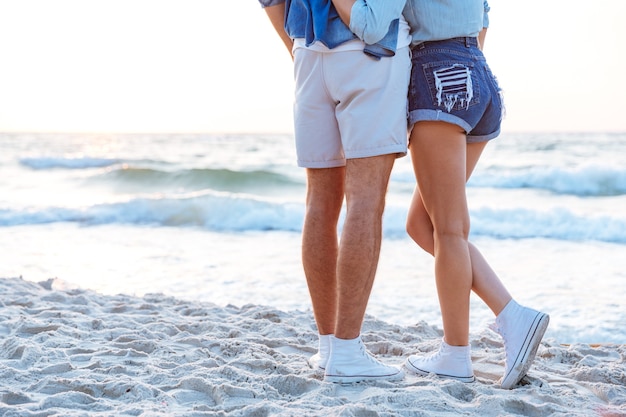 Vista posteriore delle gambe di una giovane coppia in piedi sulla spiaggia