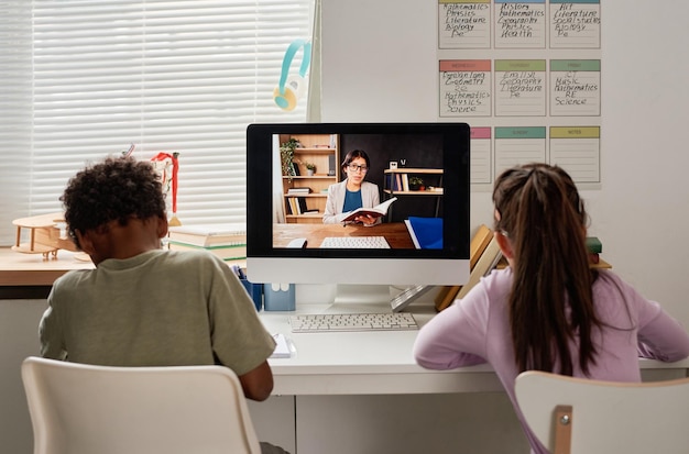 Vista posteriore di bambini di razza mista seduti a tavola e prendere appunti mentre imparano le materie scolastiche con w