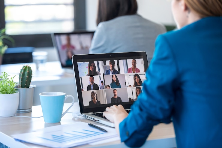 Foto vista posteriore di due donne d'affari che parlano in videochiamata con diversi colleghi durante un briefing online con un laptop in ufficio.